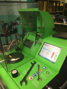 A bright green diagnostic machine with an integrated screen and two metal wrenches resting on its work surface.