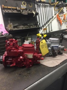A red and a silver diesel fuel injection pump sit on a workbench in front of a wall of hanging wrenches.
