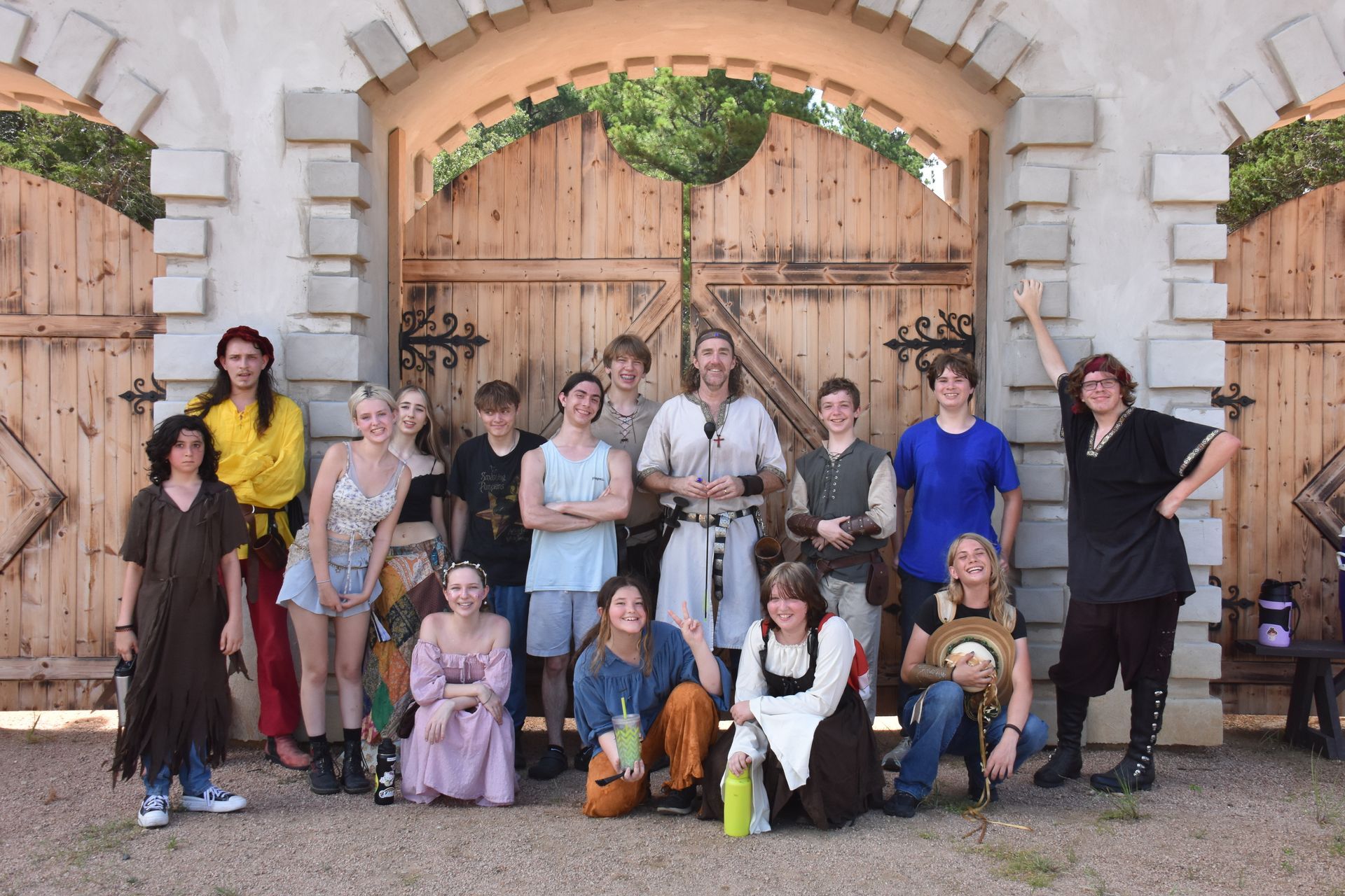 Group of costumed people pose in front of large wooden castle doors.