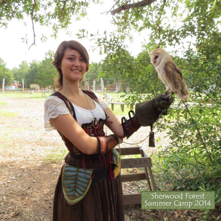 Woman in Renaissance garb smiling, holding a barn owl at Sherwood Forest Summer Camp.