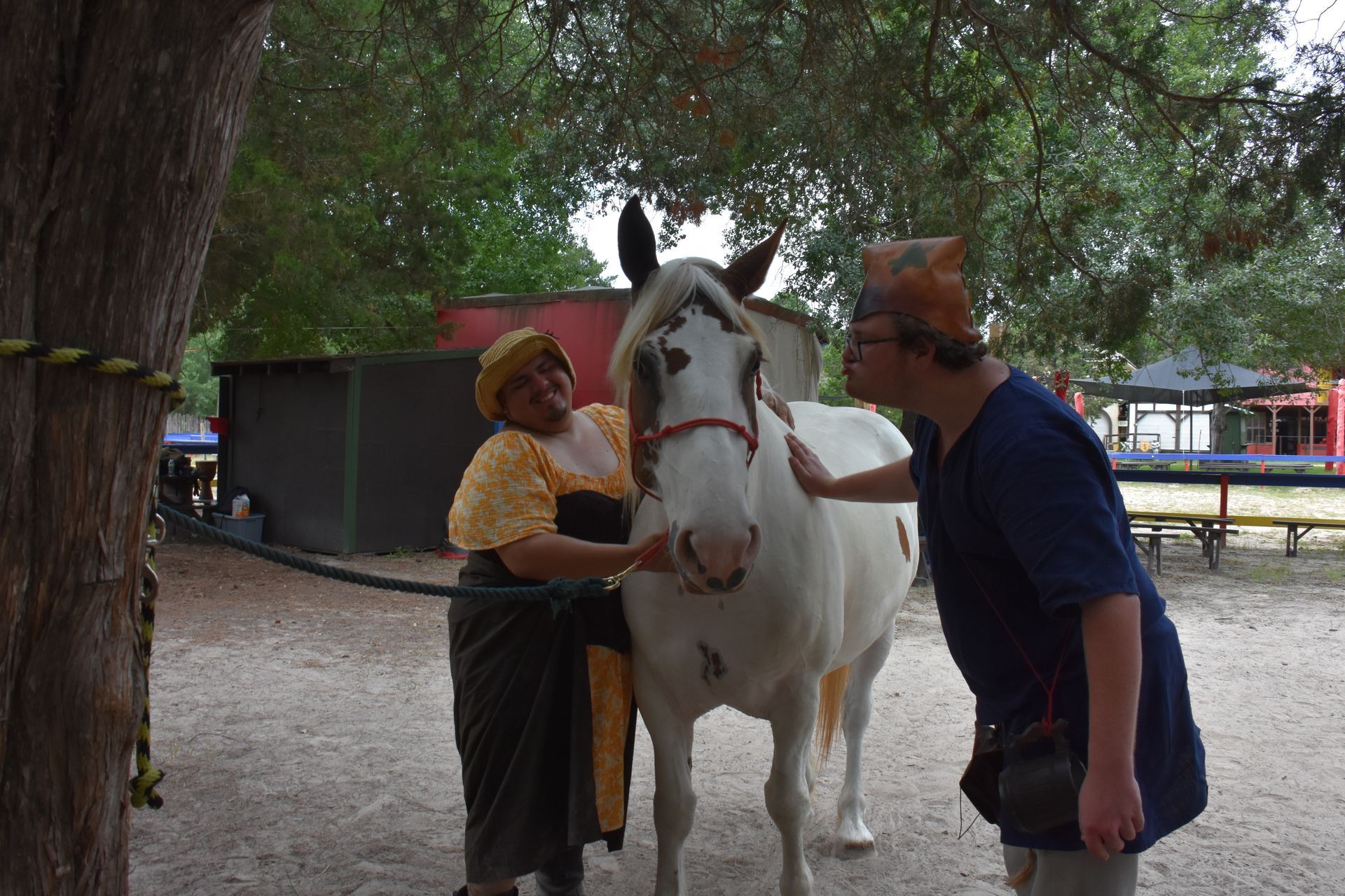 Woman and person pet a white horse with brown spots outdoors.