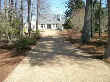 Driveway leading to a light-colored house surrounded by trees.