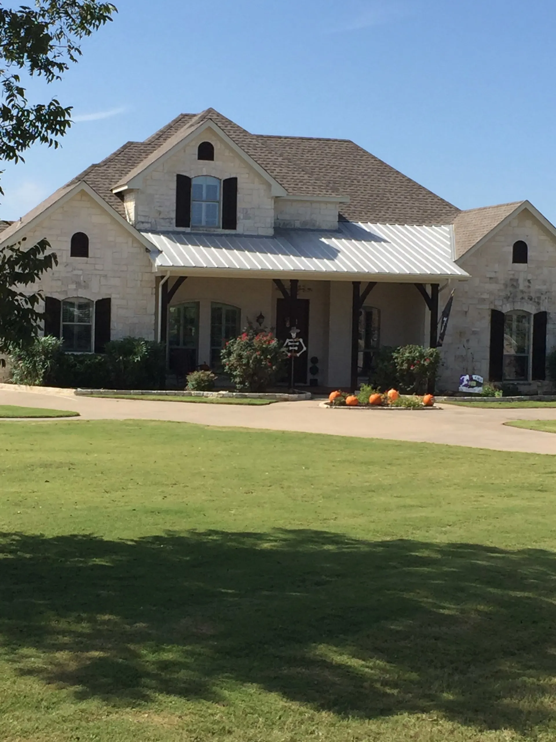 Light brick house with porch and black shutters, pumpkins sit in front.