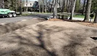 Dirt-covered ground prepared for planting, with a truck in the distance and trees in the background.