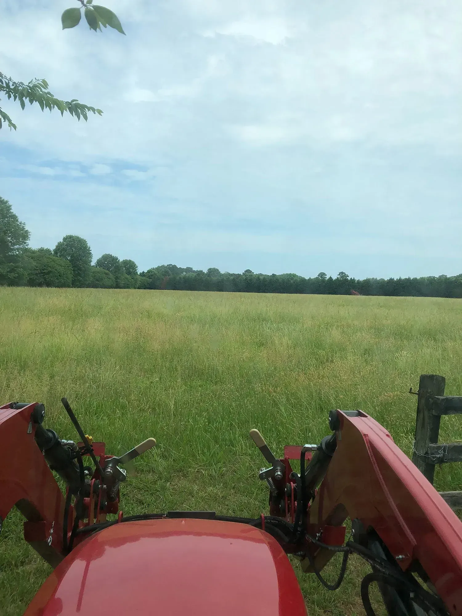 Red tractor overlooking a green field under a cloudy sky.