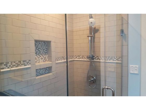 Shower with beige tiled walls, glass door, and niche with mosaic tiles. Chrome fixtures are visible.