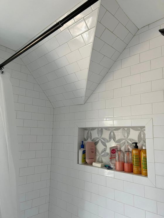 White tiled shower with a decorative inset and angled ceiling.