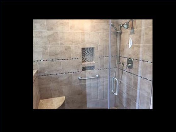 Shower with beige tiled walls, glass door, and silver fixtures; includes a built-in bench and grab bar.