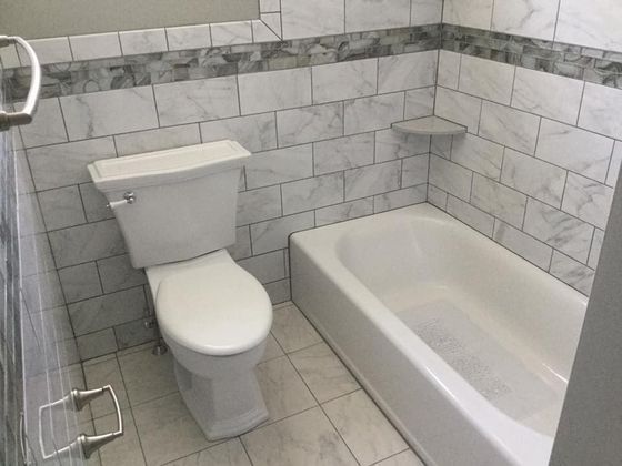 Bathroom with white toilet, tub, and tiled walls and floor. Gray accent tiles.