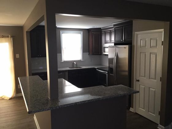 Modern kitchen with dark cabinetry, stainless steel appliances, granite countertops, and a pass-through opening.