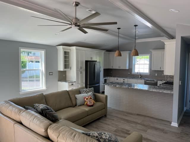 Open-concept living space with beige sectional sofa, white kitchen cabinets, and a gray granite countertop island.