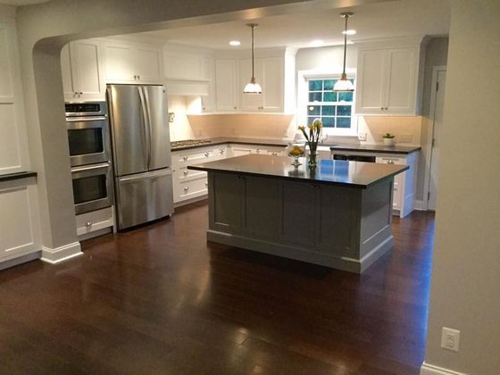 Kitchen with white cabinets, gray island, stainless steel appliances, dark wood floors.