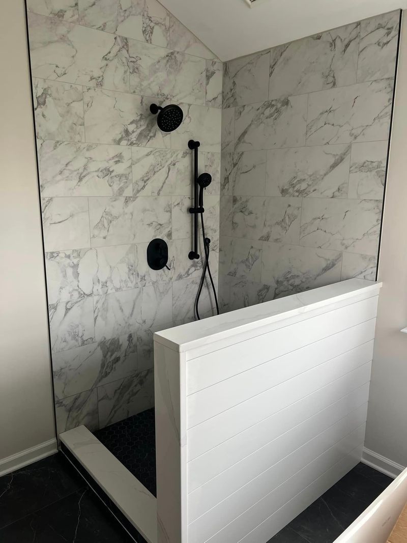 Shower with marble-patterned tile walls, black fixtures, and a white divider.