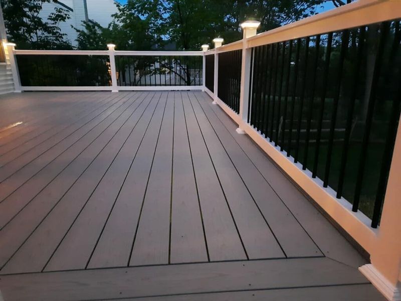 Composite deck with white and black railing, capped with lighted posts, dusk setting.