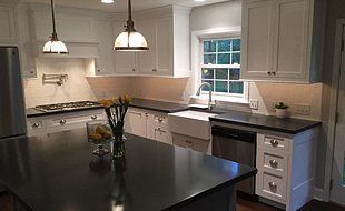 Modern white kitchen with black countertops, island, stainless steel appliances, and pendant lighting.