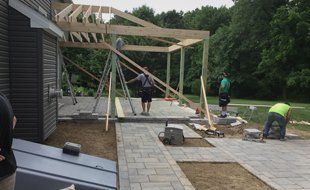 Construction of a wooden pergola on a patio, with workers using tools and standing.