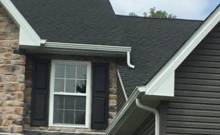 House exterior with dark roof, gutters, window, stone, and gray siding.