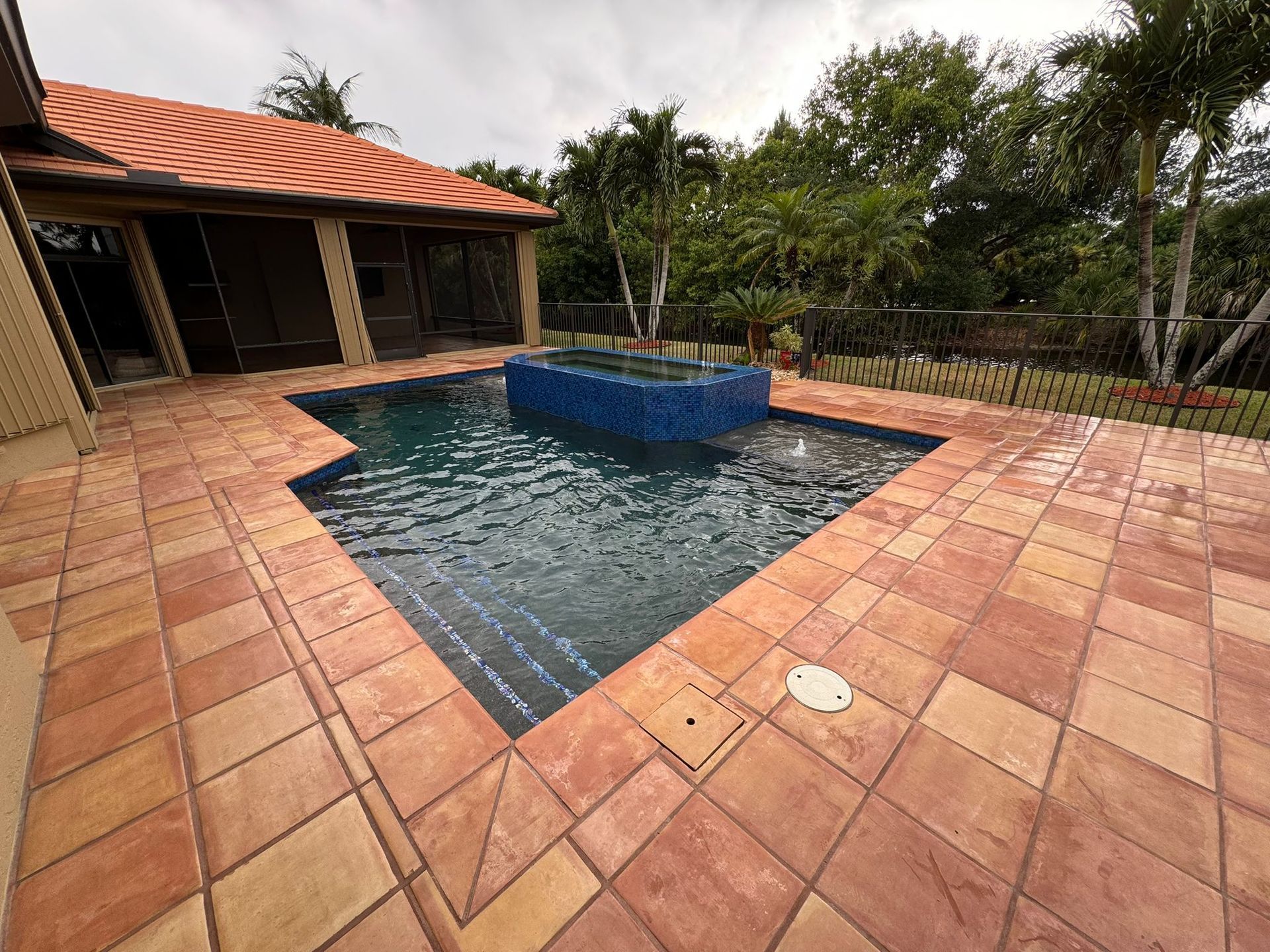 A large swimming pool is surrounded by a tiled patio and a house.