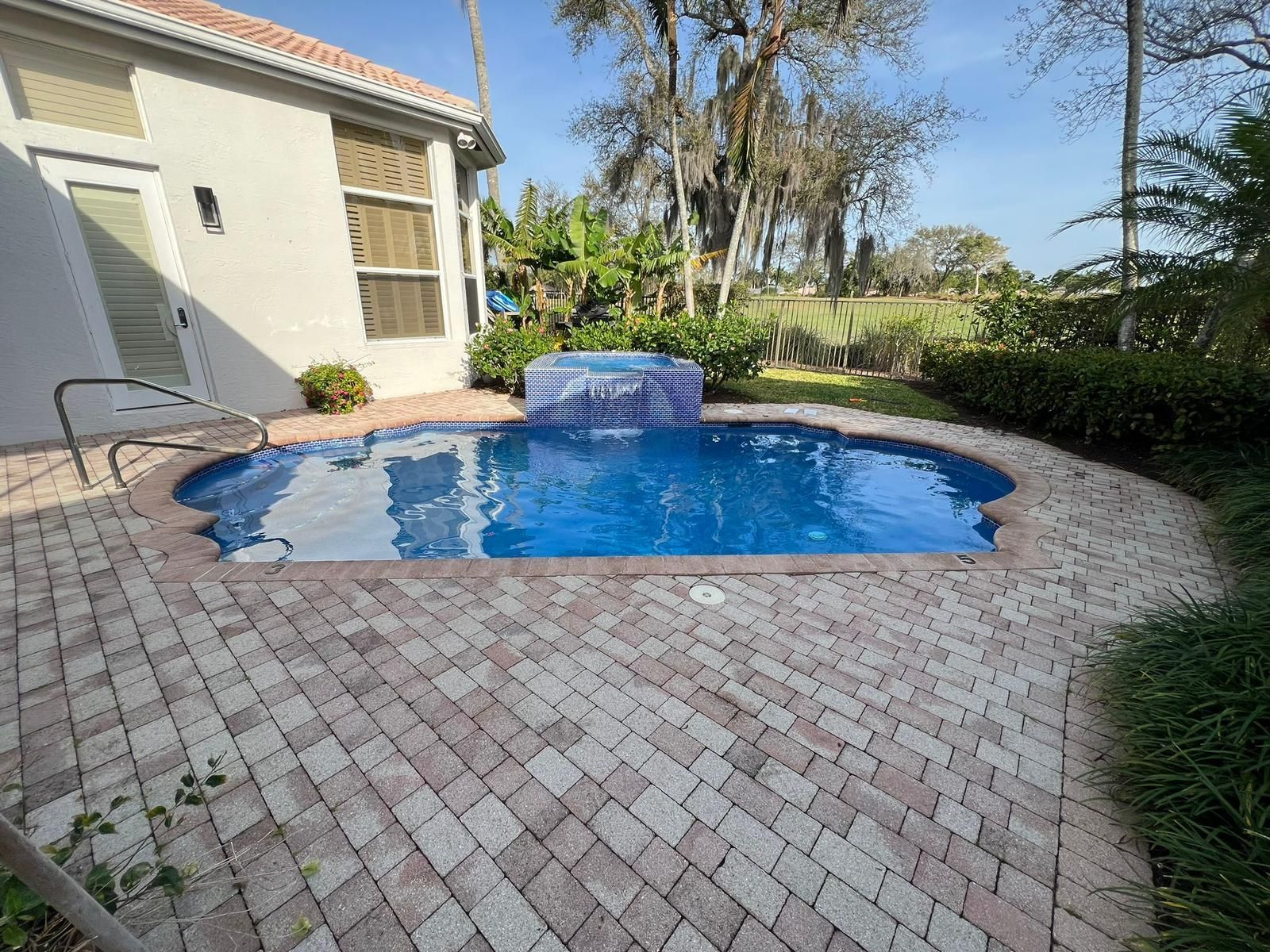 A large swimming pool is sitting on a brick patio in front of a house