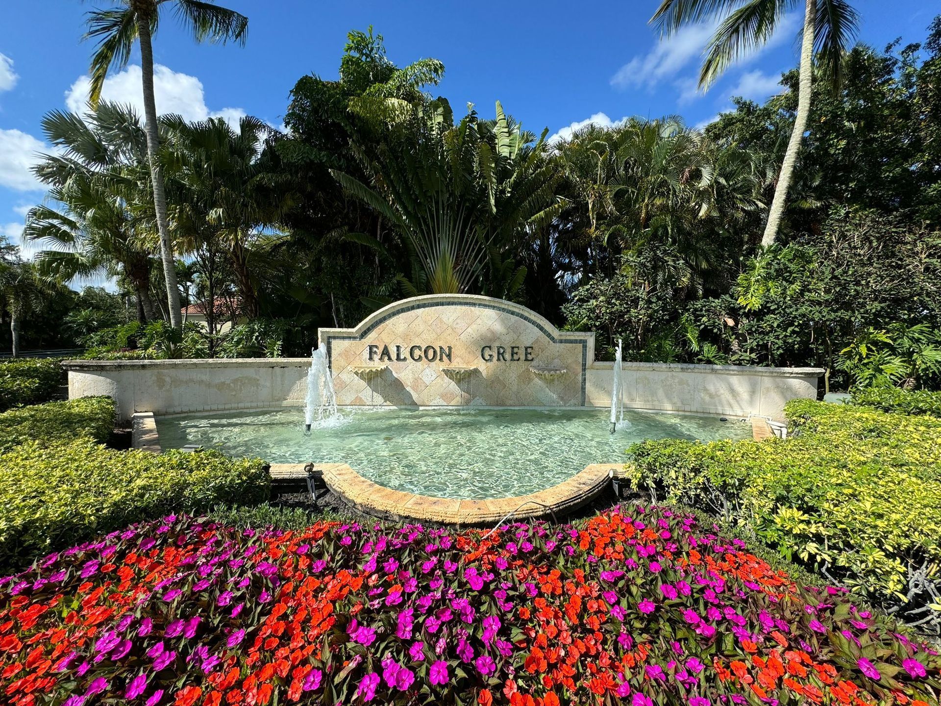 A sign for falcon creek is surrounded by flowers and palm trees.