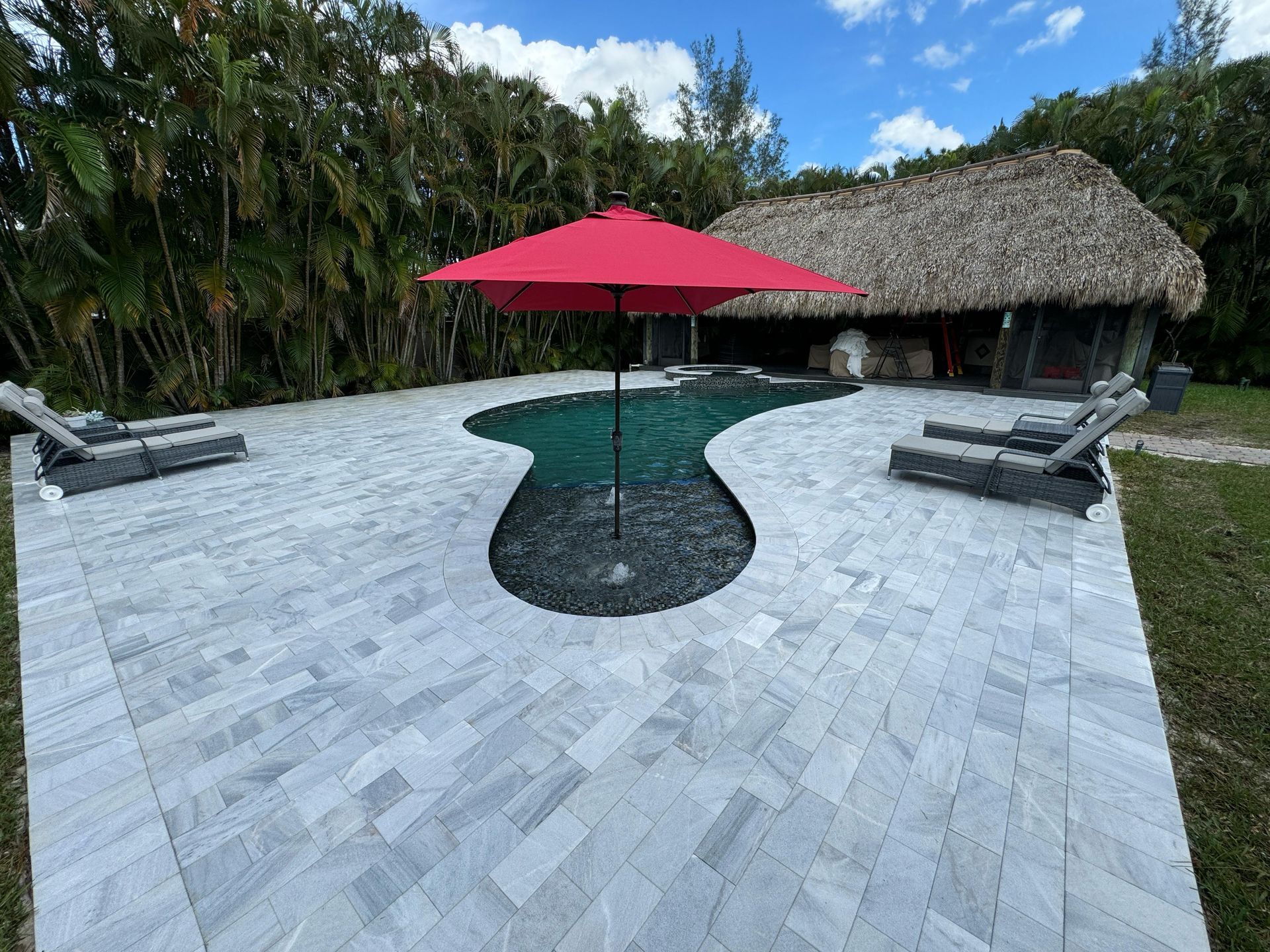 A red umbrella is sitting on a patio next to a pool.