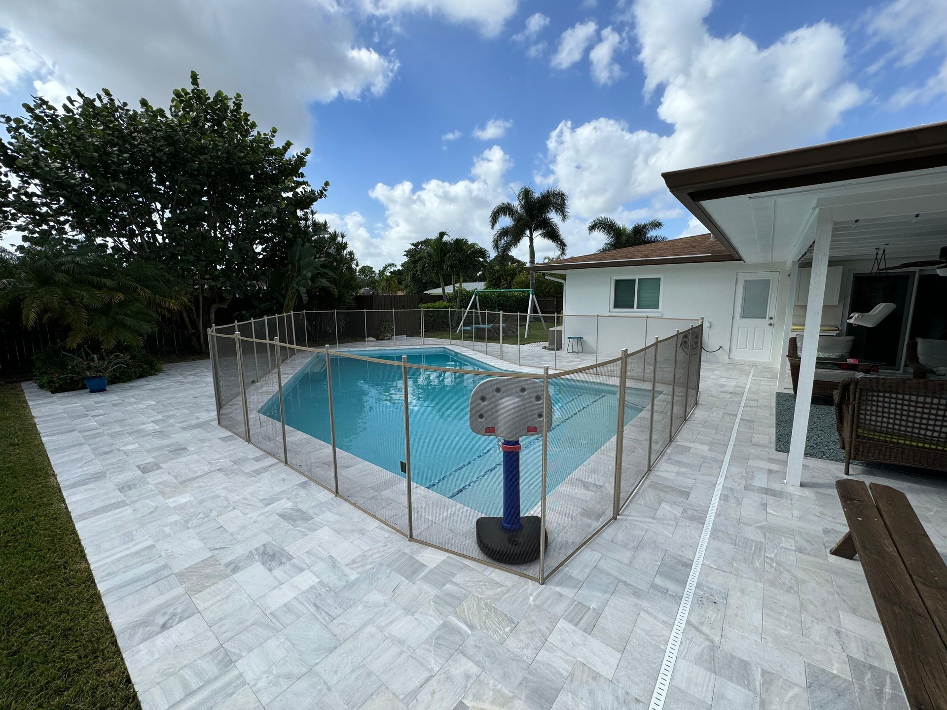 A large swimming pool surrounded by a fence and a basketball hoop.