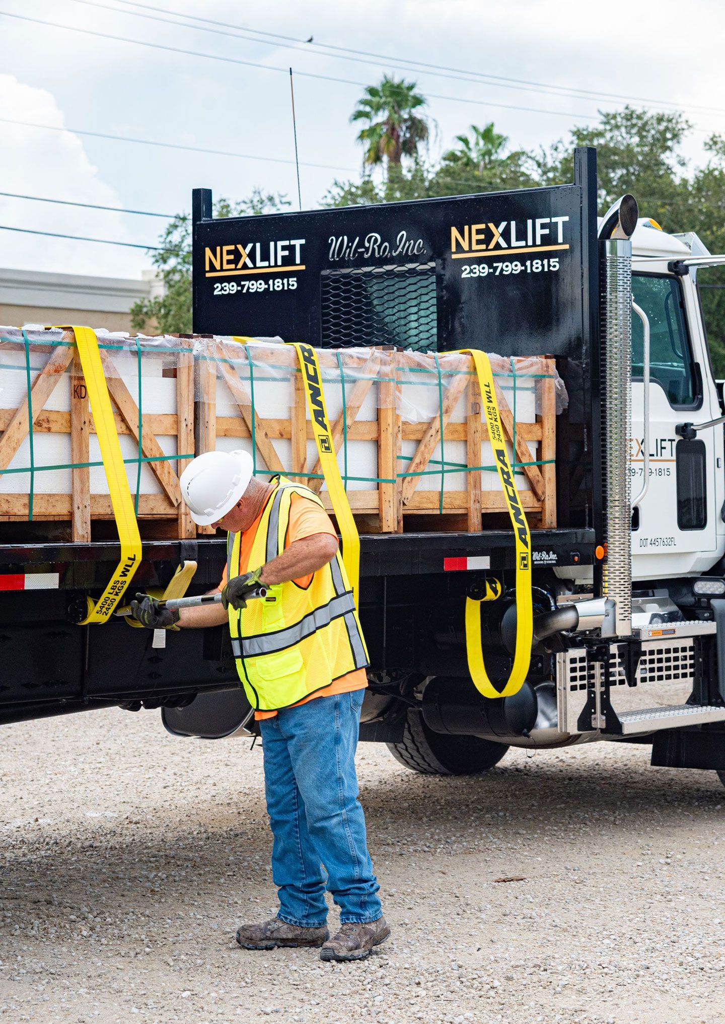 Worker in safety vest secures cargo with straps on a Nexlift truck.