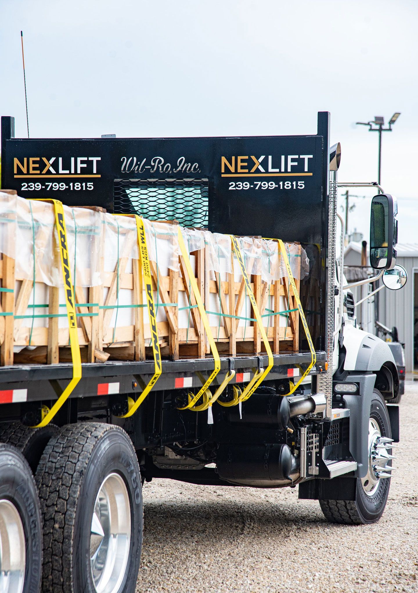 Flatbed truck loaded with wooden crates secured with yellow straps, NEXLIFT logo on the truck.