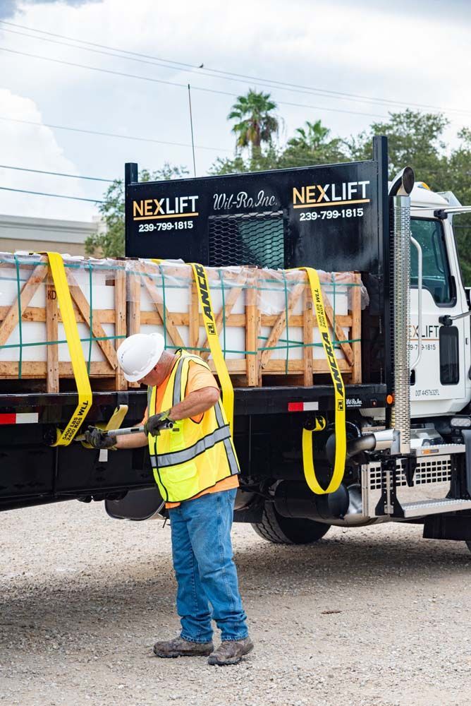 Worker secures cargo on a Nexlift truck, wearing a hard hat and safety vest outdoors.