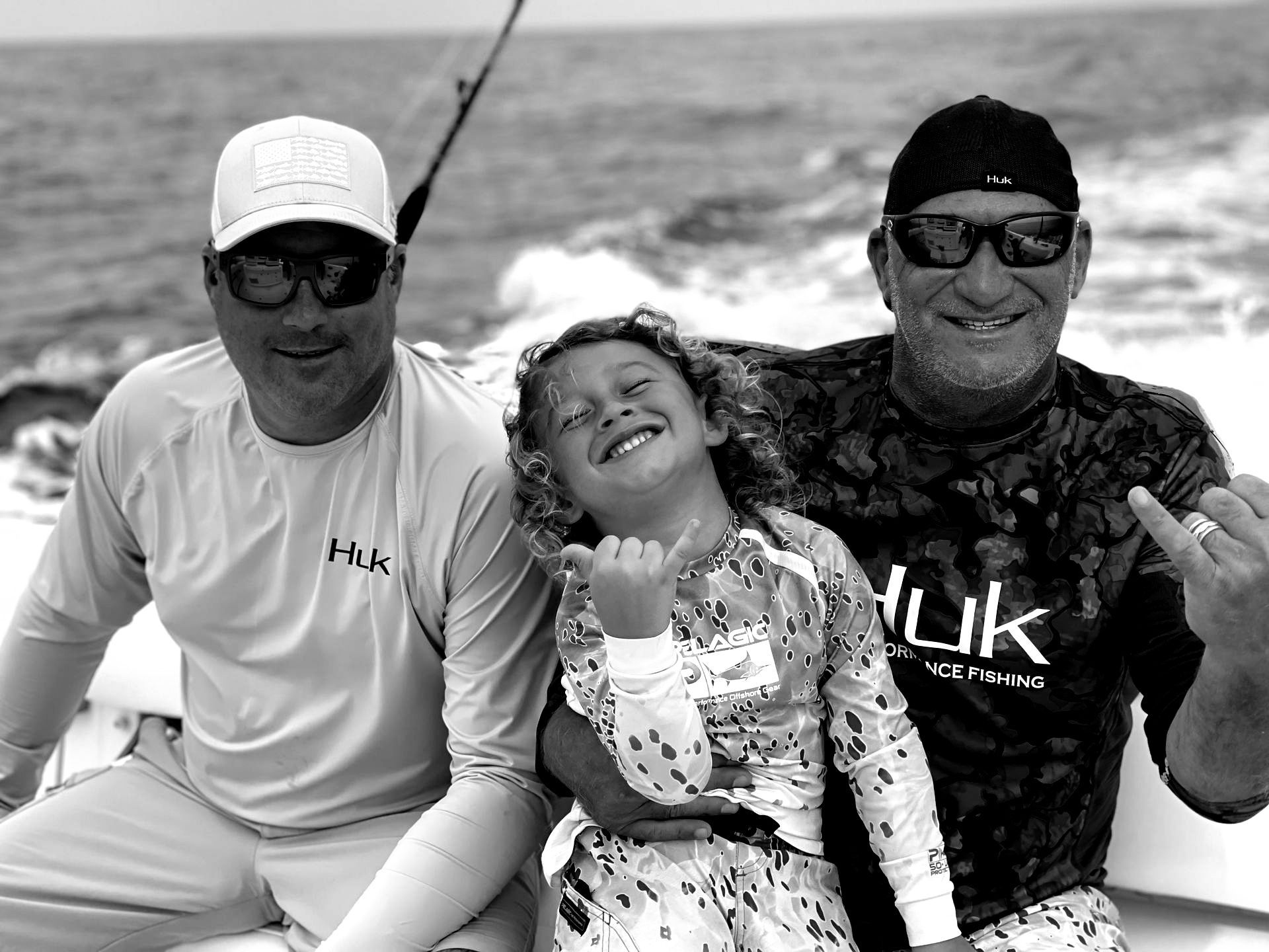 Three people on a boat: Two men and a smiling child. They are wearing sunglasses and casual clothes, with the child in the middle.