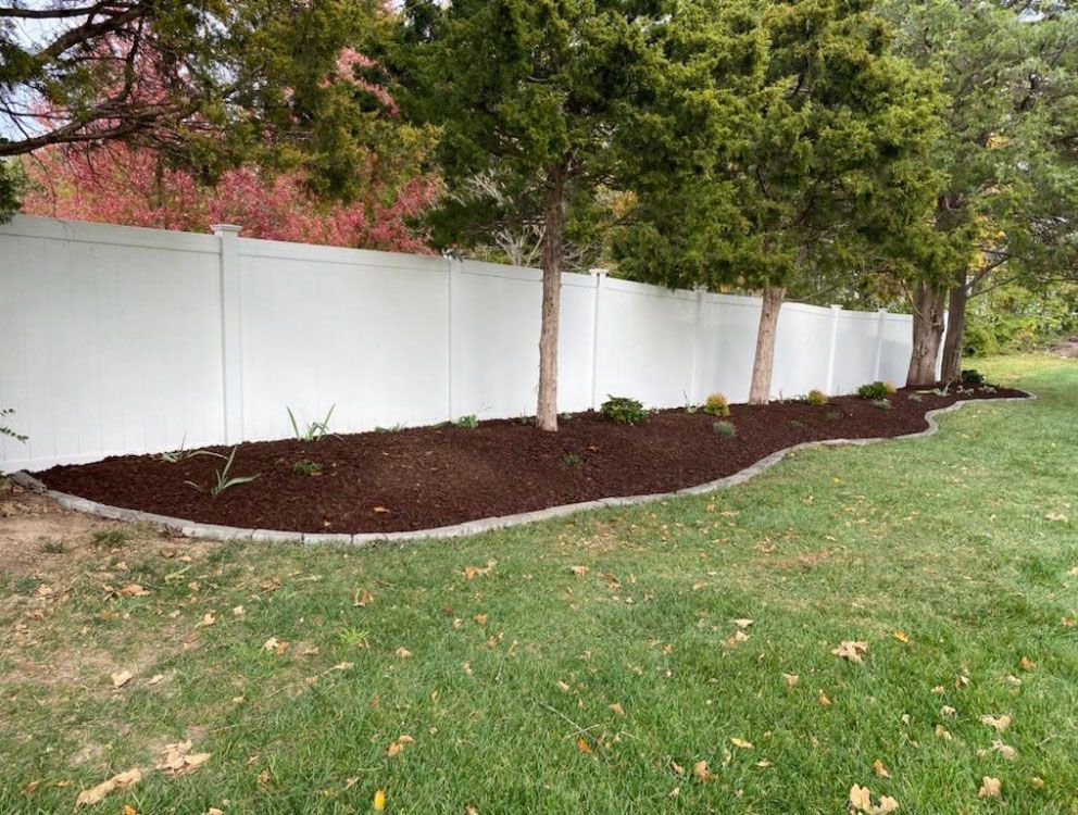 a white fence surrounds a lush green yard with trees and mulch