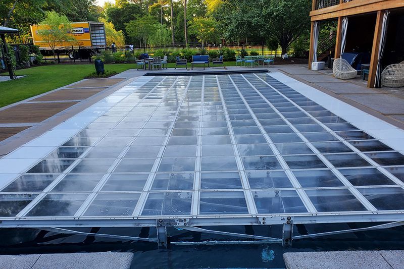 Large empty glass fountain or skylight platform in a park-like plaza, with trees and benches in the background
