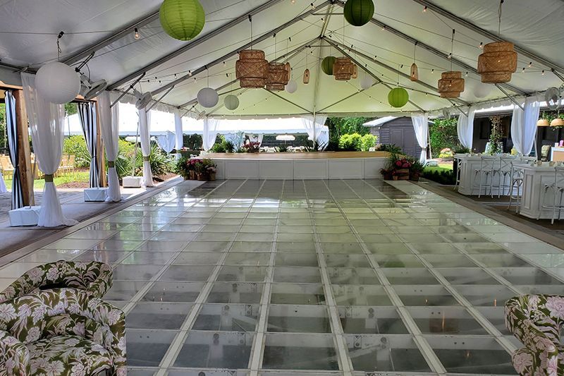 Empty decorated event tent with white drapes, hanging lanterns, and a tiled dance floor setup