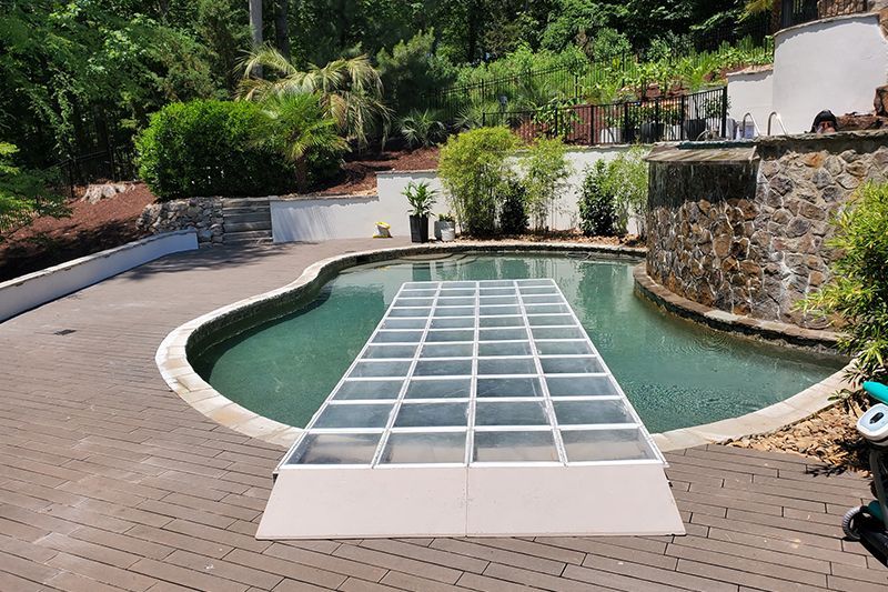 Curved backyard pool with a covered walkway and surrounding stone and wood decking