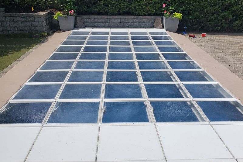 Empty outdoor swimming pool covered with blue and white safety tiles, surrounded by patio
