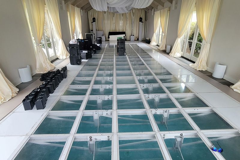 Long glass-floor walkway inside a draped event tent with white seating along both sides