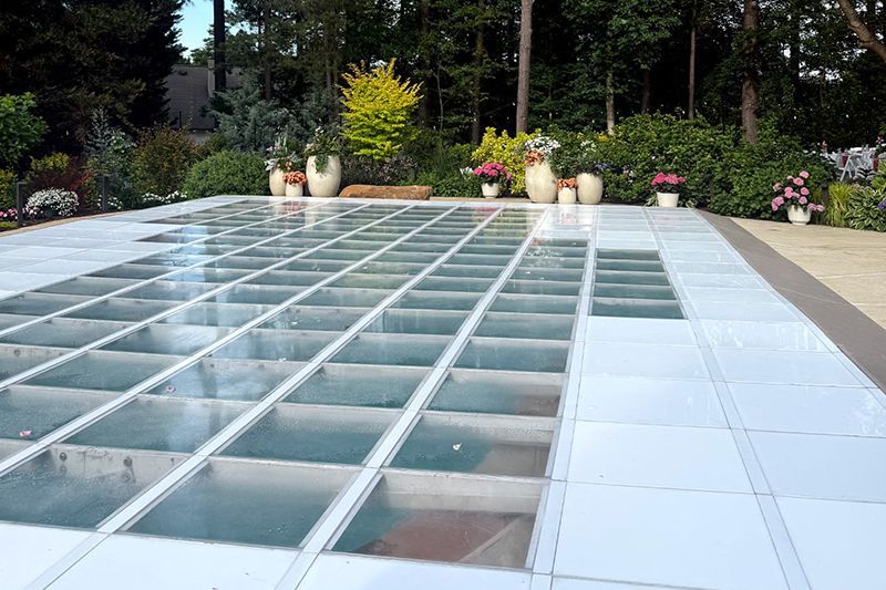 Glass-roofed patio beside a garden with potted flowers and greenery