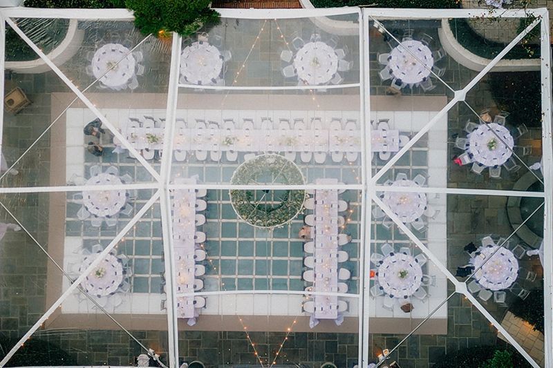 Overhead view of an outdoor event setup with white round tables and chairs in a tiled courtyard