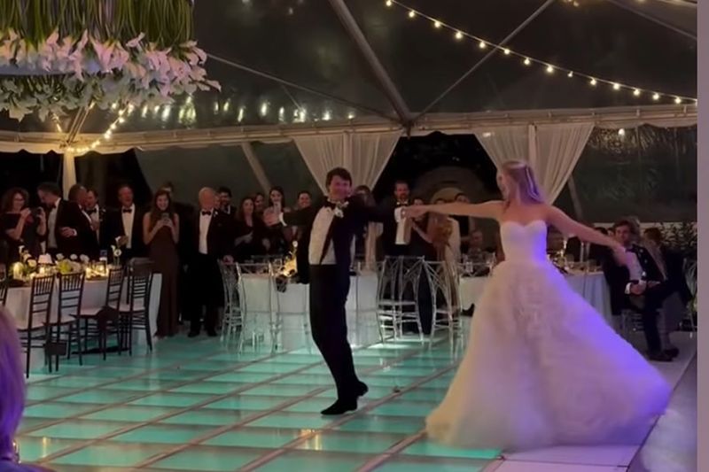 Bride and groom dancing at a nighttime wedding reception under string lights and a tented ceiling