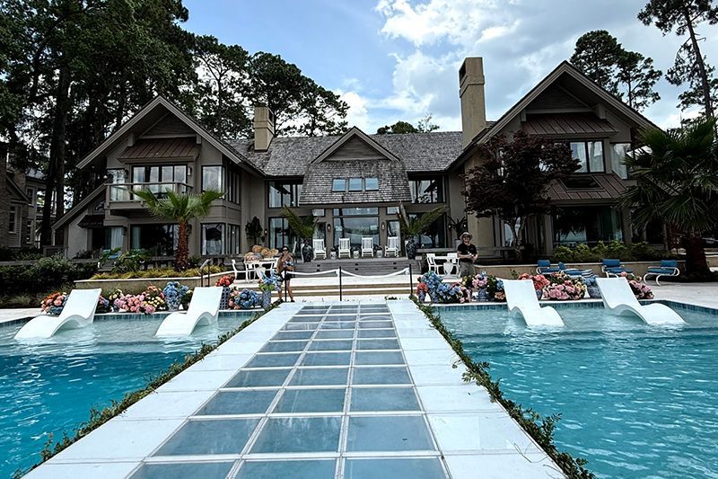 Luxury resort pool with a glass walkway leading to a large lodge and lounge chairs by turquoise water
