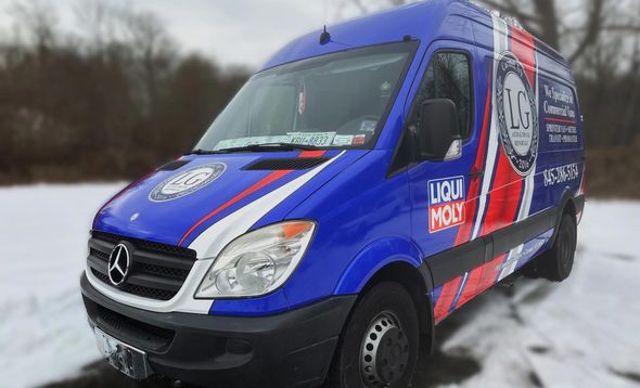 White Mercedes van with hood up in a garage, being worked on. Diagnostic equipment is visible.