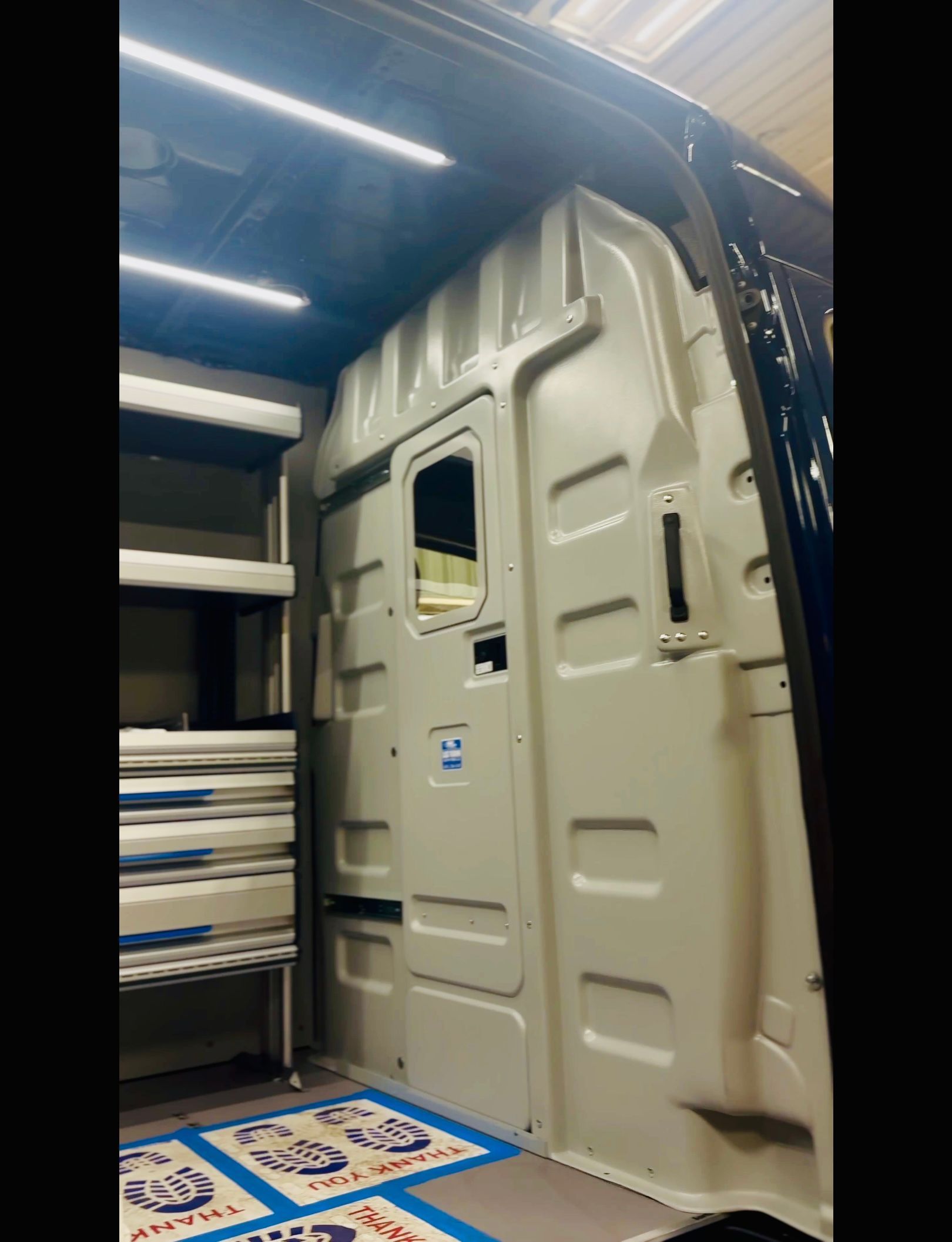 A red and white Volkswagen bus is lifted on a car lift in a garage.