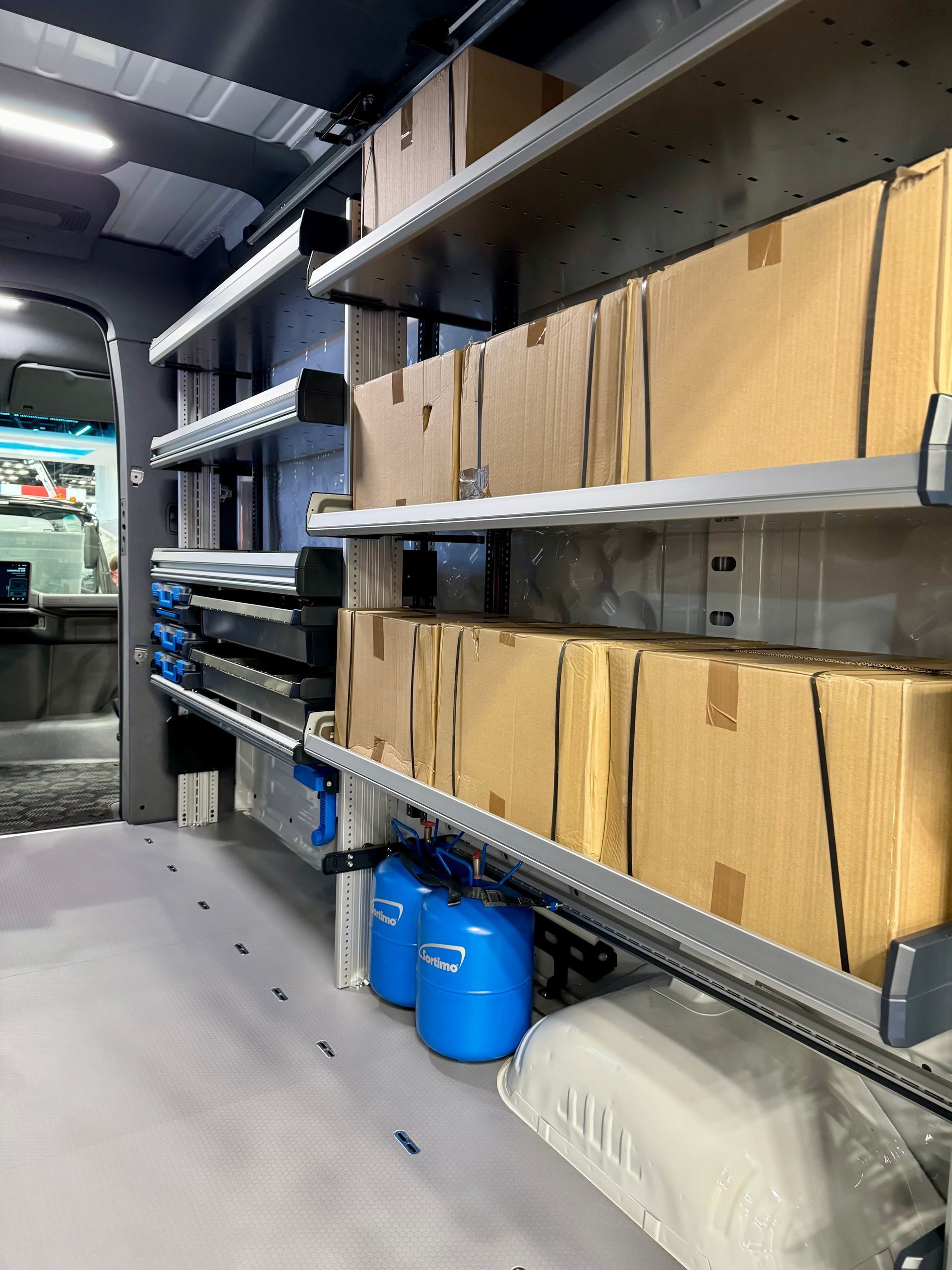 Van interior with shelving holding cardboard boxes and blue containers.