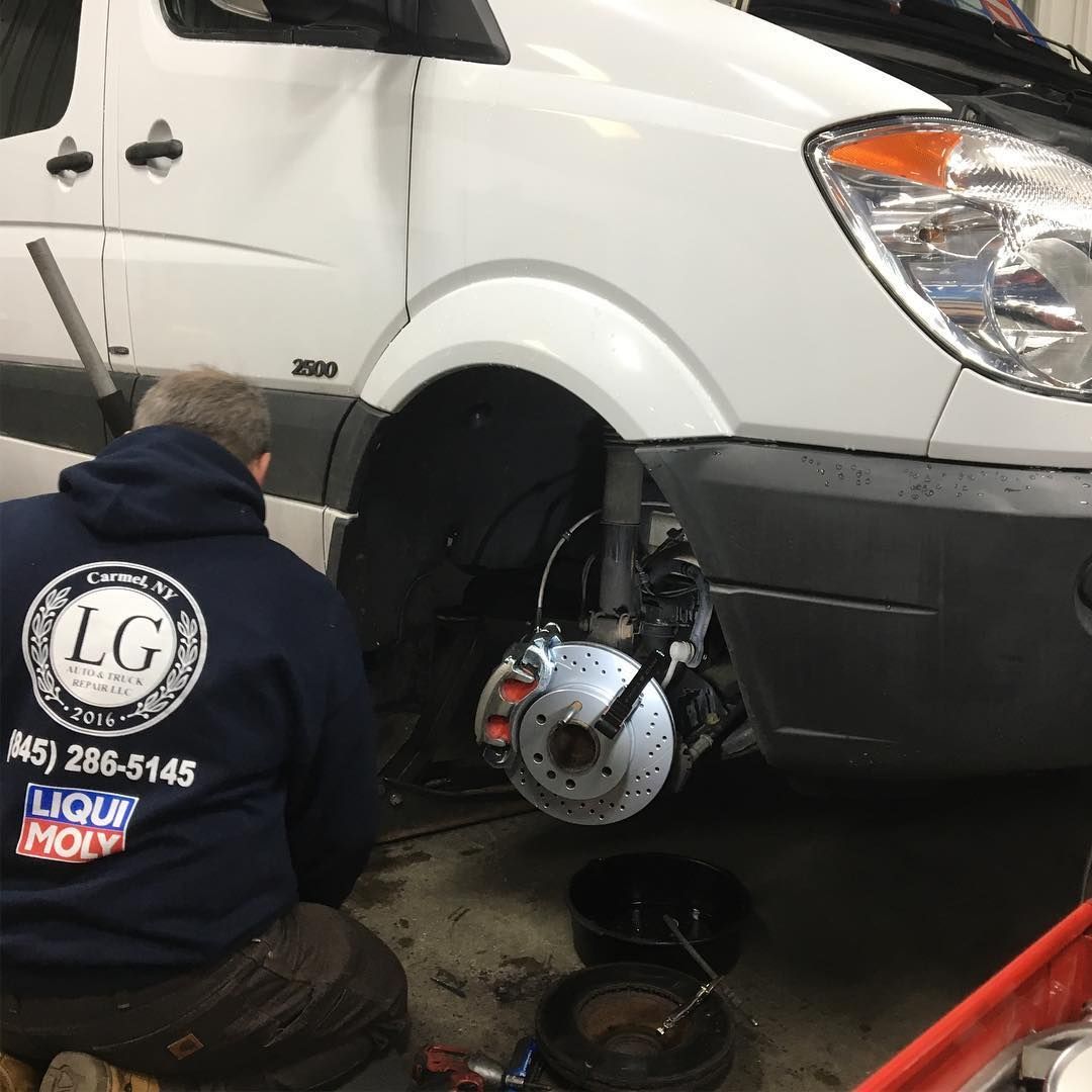 Mechanic working on the front brakes of a white van in a garage; red calipers visible.