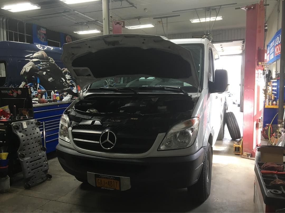 White Mercedes Sprinter van with open hood in a repair shop.