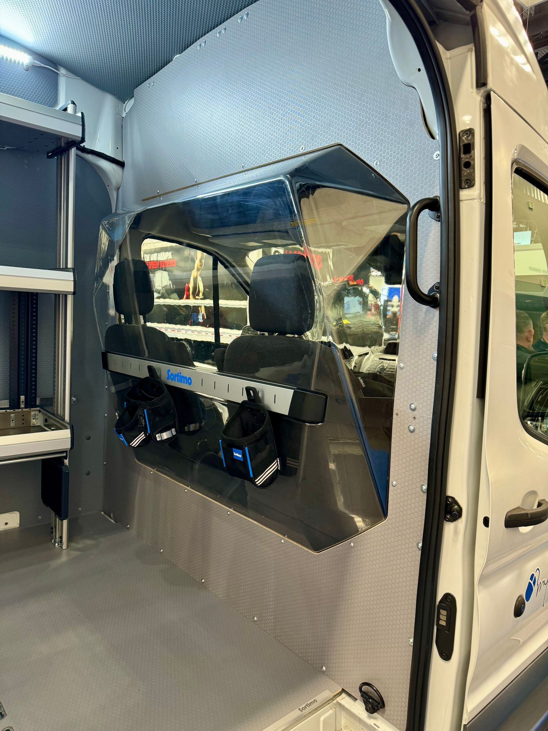Interior of a van with partition wall, seats, and equipment storage. Silver metal paneling.