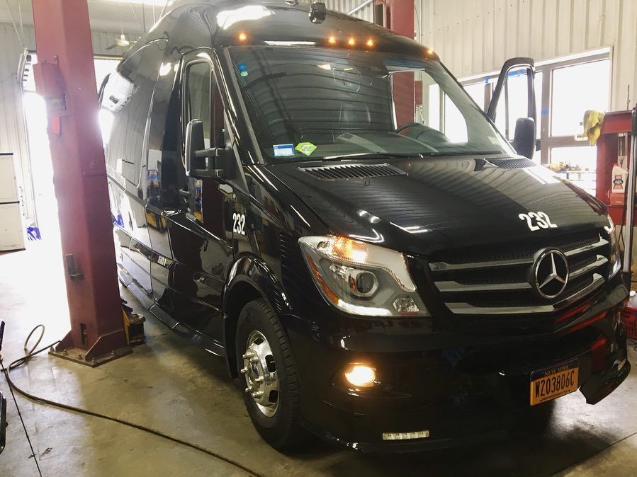 Black Mercedes-Benz Sprinter van in a garage with the door open and a red lift supporting it.