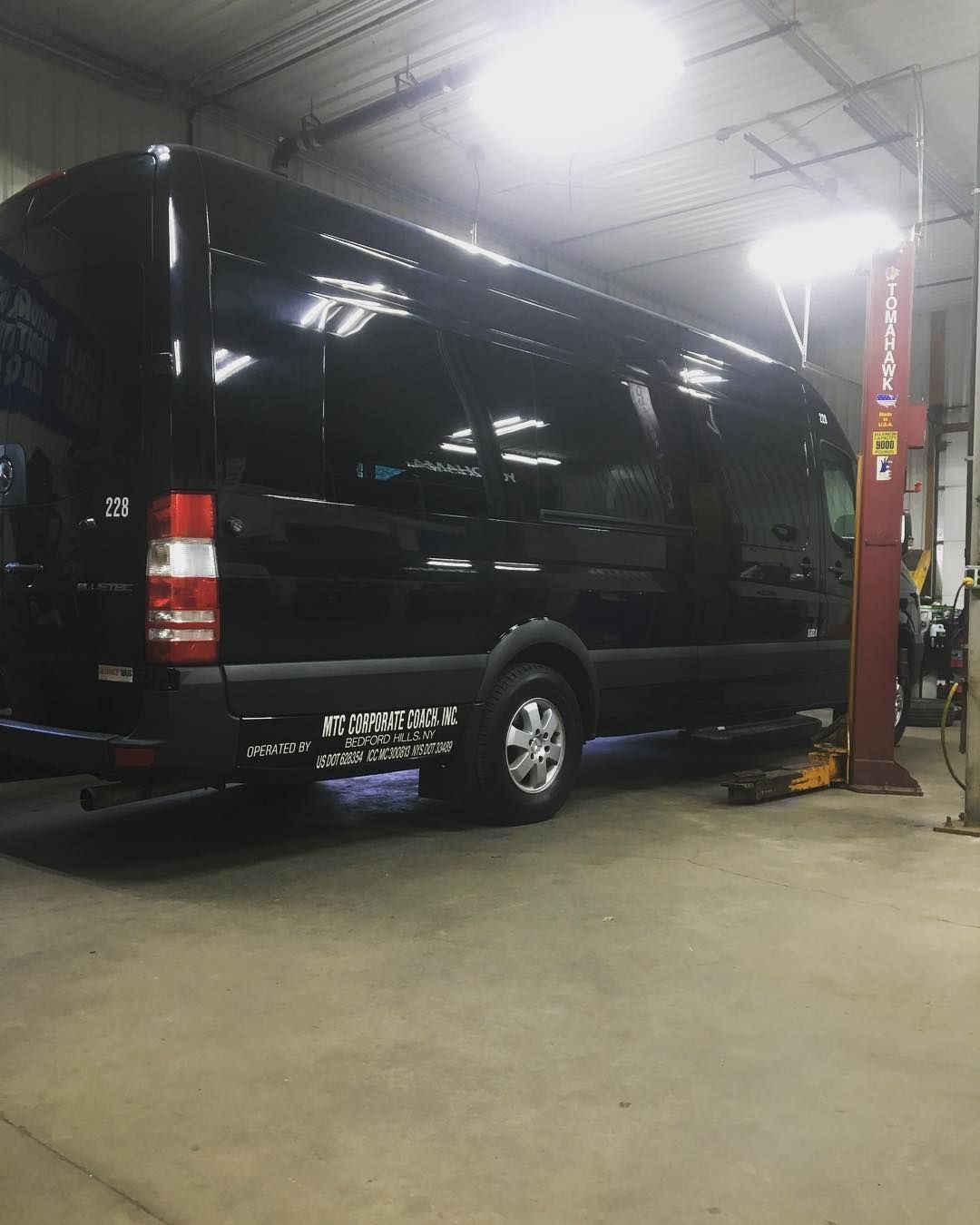 Black van inside a garage, possibly under repair. Red lift post to the right.