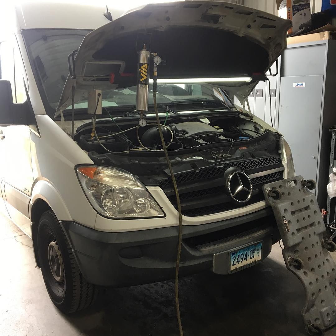 White Mercedes Sprinter van with open hood in a garage, undergoing repair.