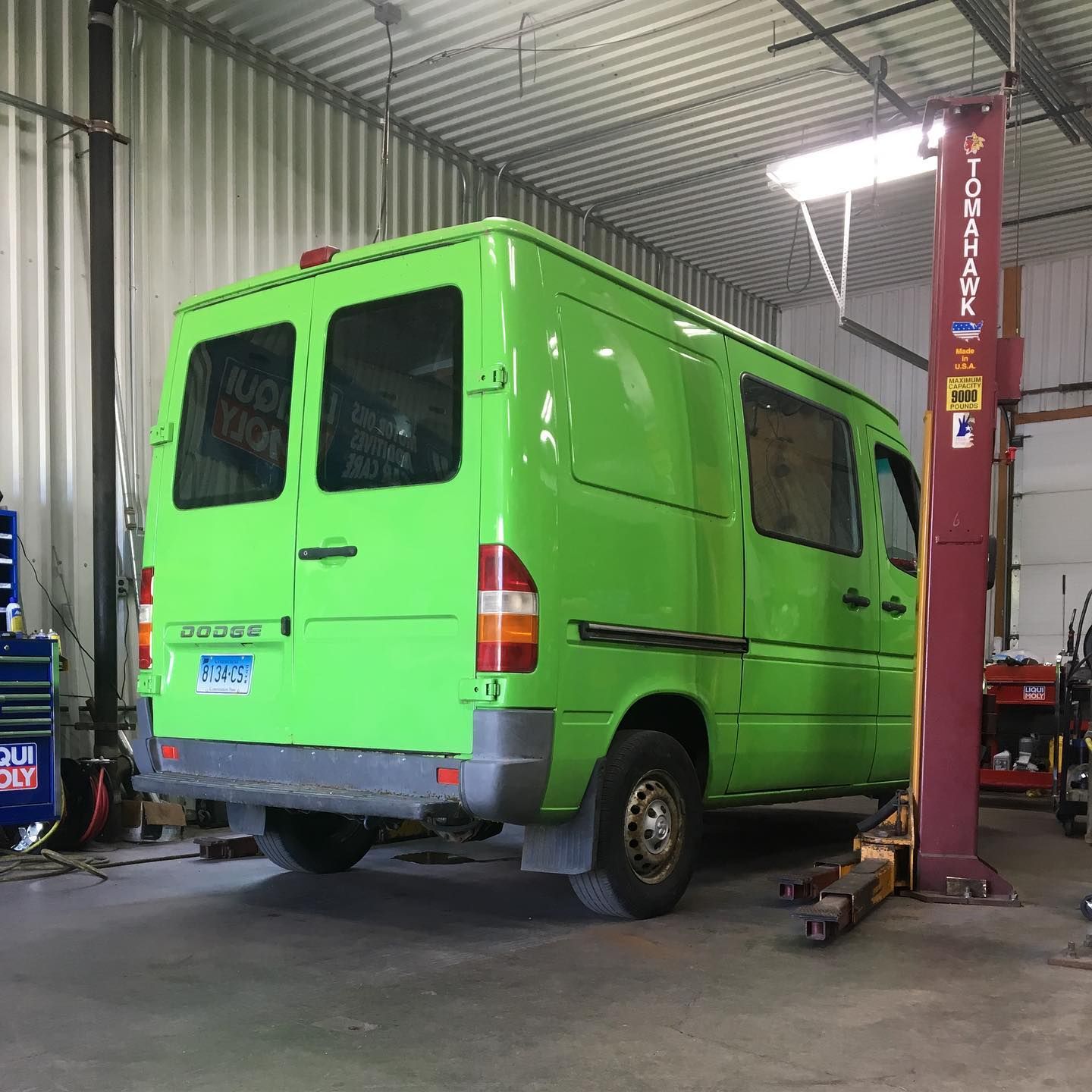 Green van on a lift inside a garage.